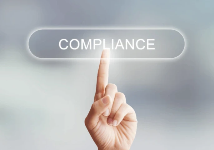A hand pressing a button with the words "COMPLIANCE" on it.