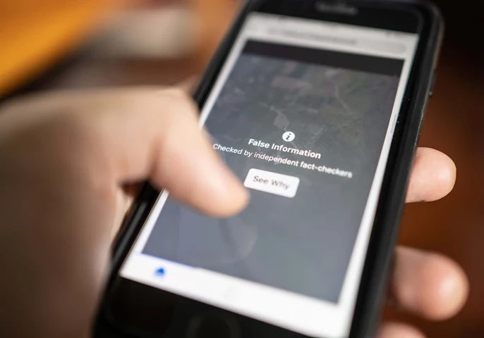 A person's hand holding a phone where the screen is displaying a message "False information"