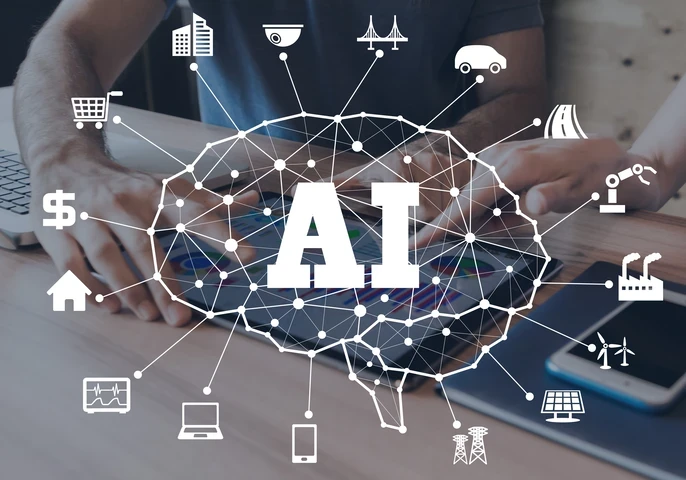 Image depicting various technology-related icons around a brain and the letters "AI" against a background of people using a tablet at a desk.