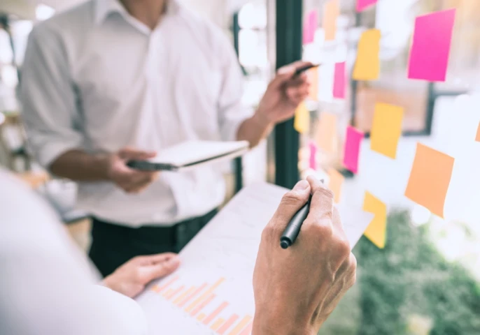 Two businesspeople standing in front of plexiglass with sticky notes discussing graphs.