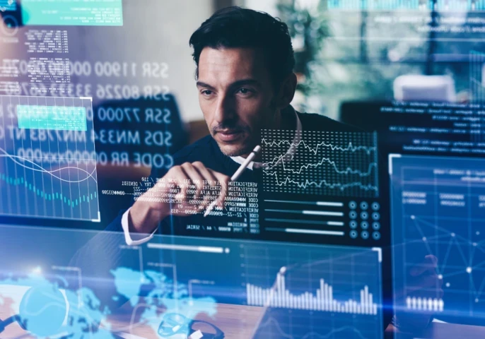 A man sitting in front of a transparent screen with code and graphics on it.