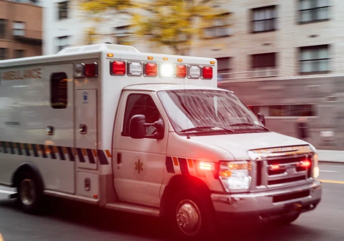 Ambulance driving down a city road with sirens and lights on.
