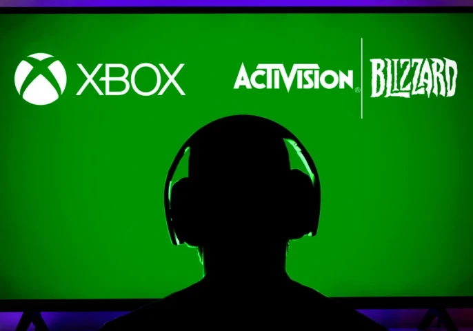 Silhouette of a person with headphones on in front of a green TV screen displaying logos from XBox, Activision and Blizzard.
