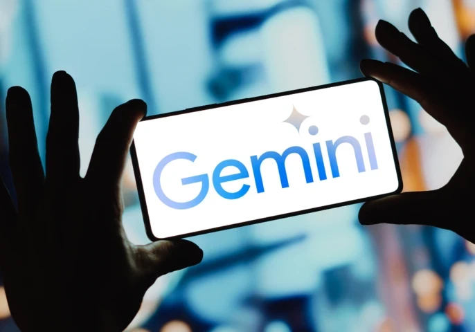Person holding up a smartphone and the screen is displaying the Google Gemini logo against a Bokeh background.