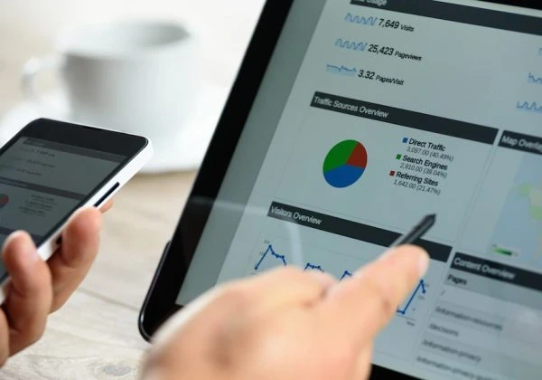 Person using a smartphone and pointing at a screen with charts on it.