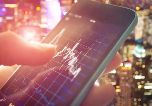 Someone using a smartphone checking stocks with a graph on a downward trend