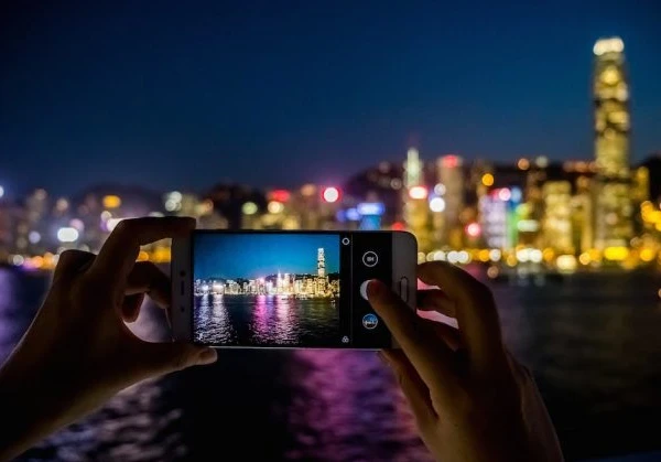 Person taking a photo using a smartphone of a China city skyline across the river at night