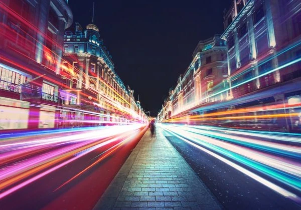 Person walking down Oxford Street with lights beaming past on either side