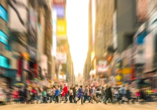 People crossing a busy road by Times Square in New York City, with a blurry cityscape background