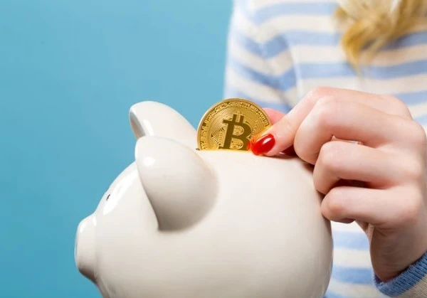 Woman placing a Bitcoin coin into a piggy bank.