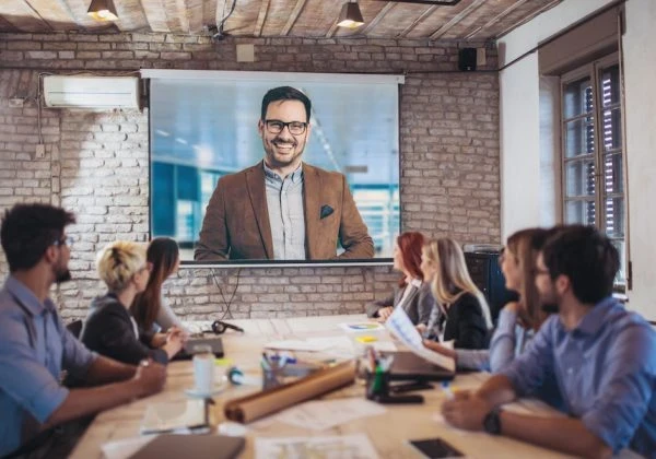 People sitting at a desk looking up at at video conferencing screen.