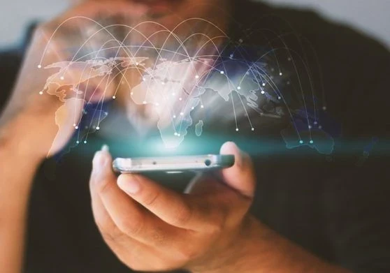 A person holding a smartphone while a graphic of the world's countries floats above the screen with various connecting lines from country to country
