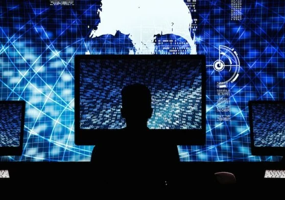 Hacker working on a large computer with additional screens next to them and a very large screen in front