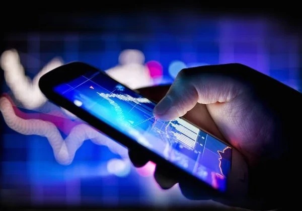 Hand holding a lit up smartphone with graphs on the screen in purple and blue.