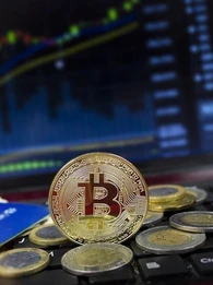 Cryptocurrency coins stacked on a keyboard in front of a screen showing stocks.