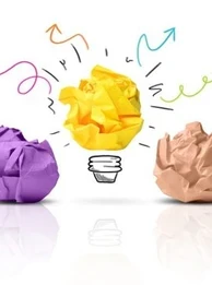 Colourful rolled up balls of paper laid out on a white table with one turning into a lightbulb.