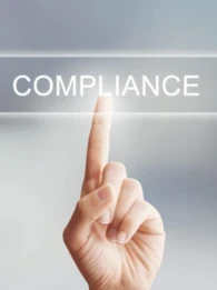 A hand pressing a button with the words "COMPLIANCE" on it.