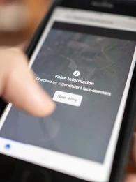 A person's hand holding a phone where the screen is displaying a message "False information"