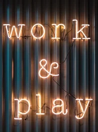 Neon lights spelling out "work & play" on a corrugated iron backdrop.