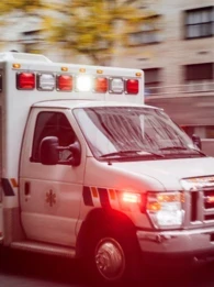 Ambulance driving down a city road with sirens and lights on.
