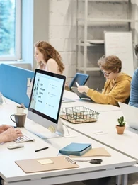 Employees sat at a large desk working on computers in a modern office