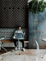 Man sitting in a cafe working on his laptop and holding a smartphone.