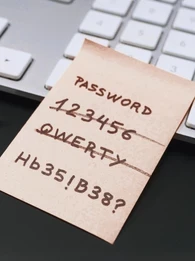 Post-It note stuck to an Apple keyboard scratching off weak passwords and ending off on a strong password.
