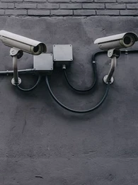 Two surveillance cameras mounted to a gray wall.