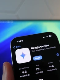 google gemini  app store screen on iphone in front of computer monitor with blue screensaver