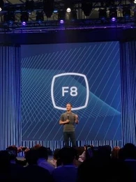 Mark Zuckerberg on stage presenting with the Facebook logo behind him.