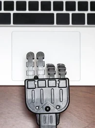 Robot hand using a trackpad on a laptop.