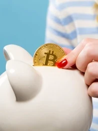 Woman placing a Bitcoin coin into a piggy bank.