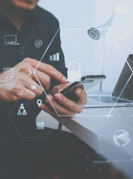 person on a smartphone next to two laptops