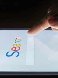 'Search' written in Google font and colours on a touchscreen with a user tapping the search bar
