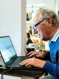 An elderly man sitting in front of a laptop.