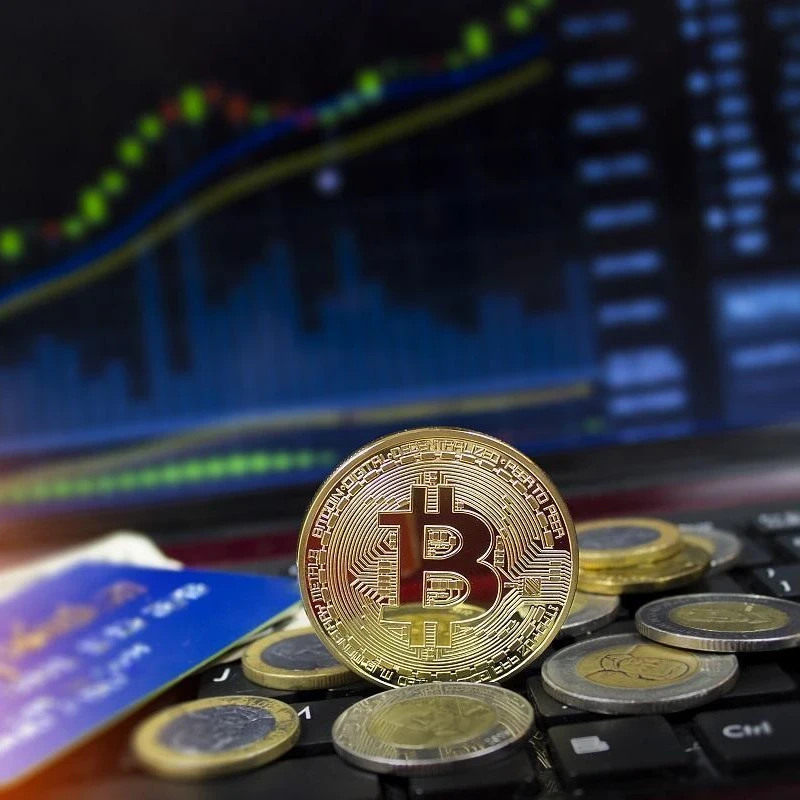 Cryptocurrency coins stacked on a keyboard in front of a screen showing stocks.