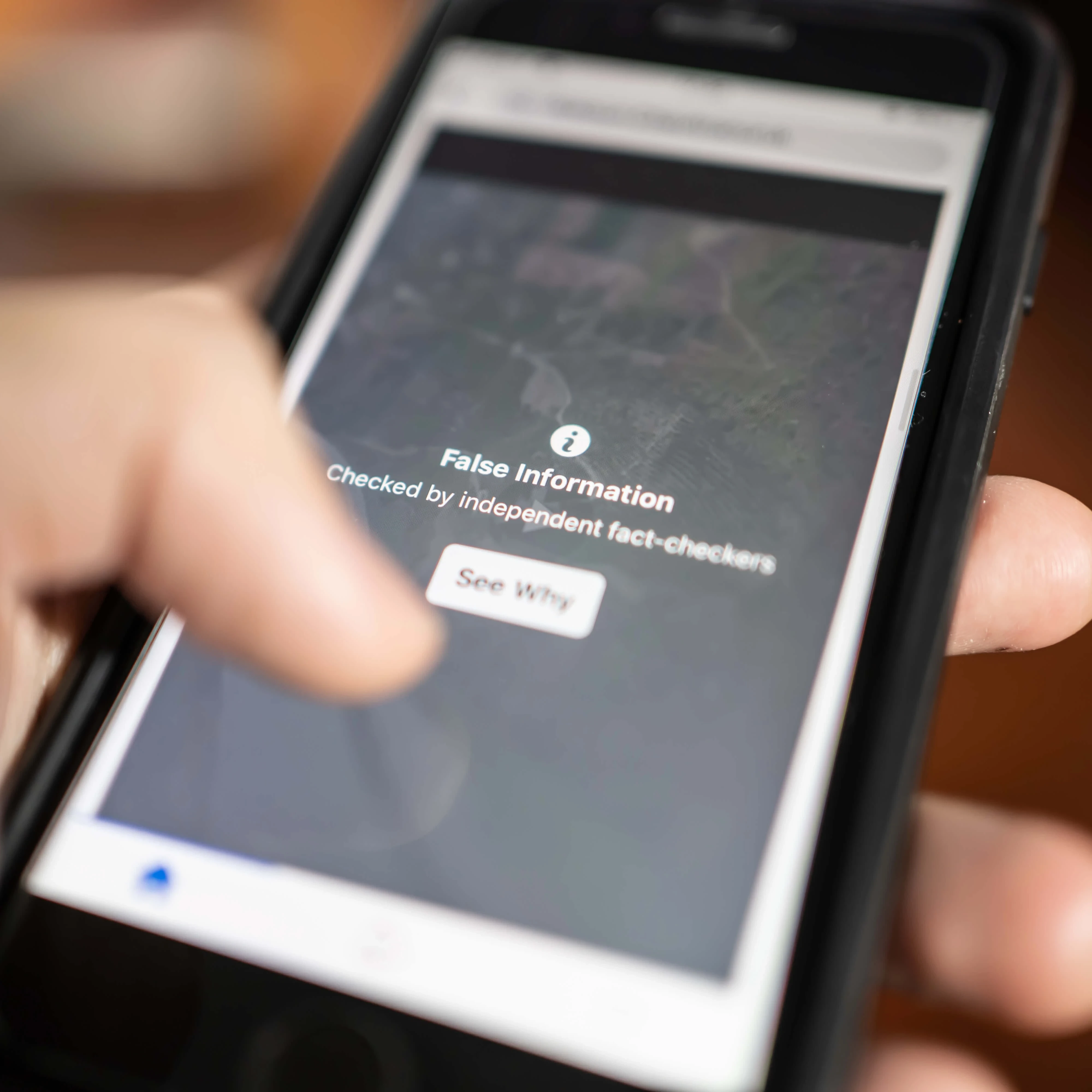 A person's hand holding a phone where the screen is displaying a message "False information"