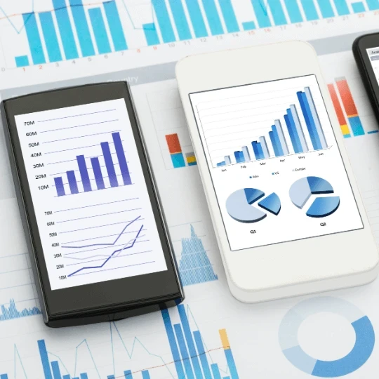 Three smartphone laid on top of a pile of paper graphs.