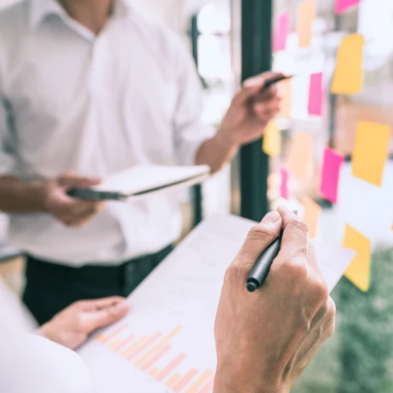Two businesspeople standing in front of plexiglass with sticky notes discussing graphs.