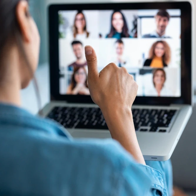 A woman sitting in front of a laptop on a video meeting giving a thumbs up.
