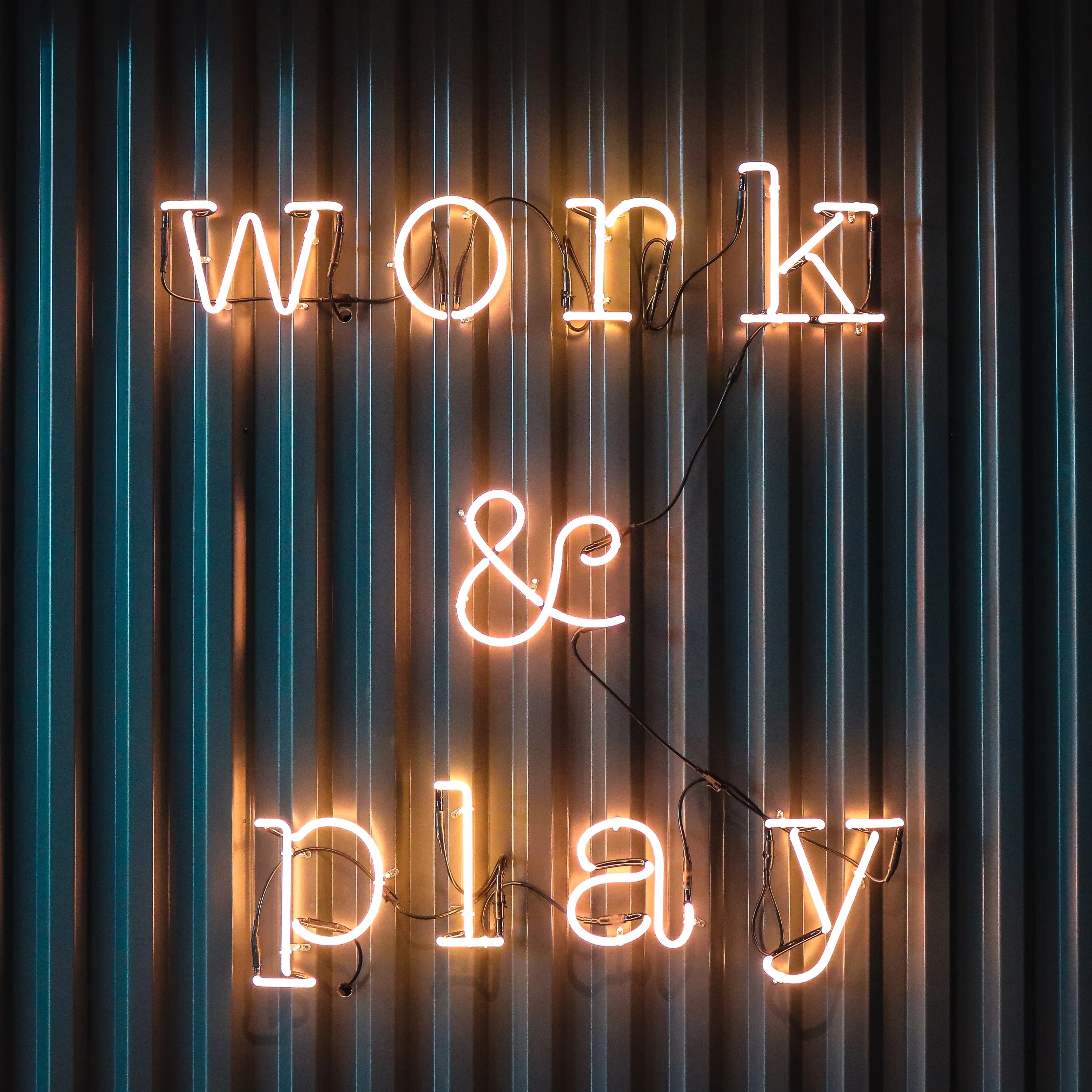 Neon lights spelling out "work & play" on a corrugated iron backdrop.