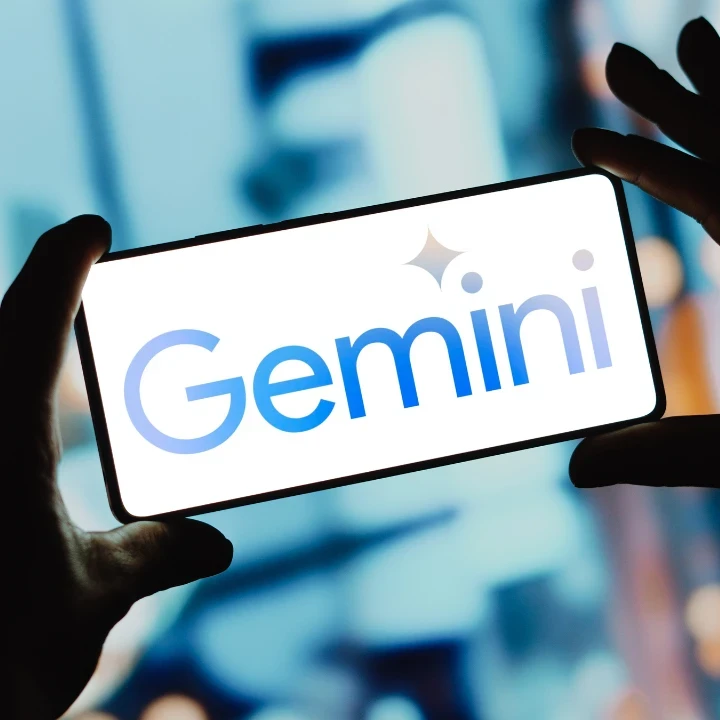 Person holding up a smartphone and the screen is displaying the Google Gemini logo against a Bokeh background.