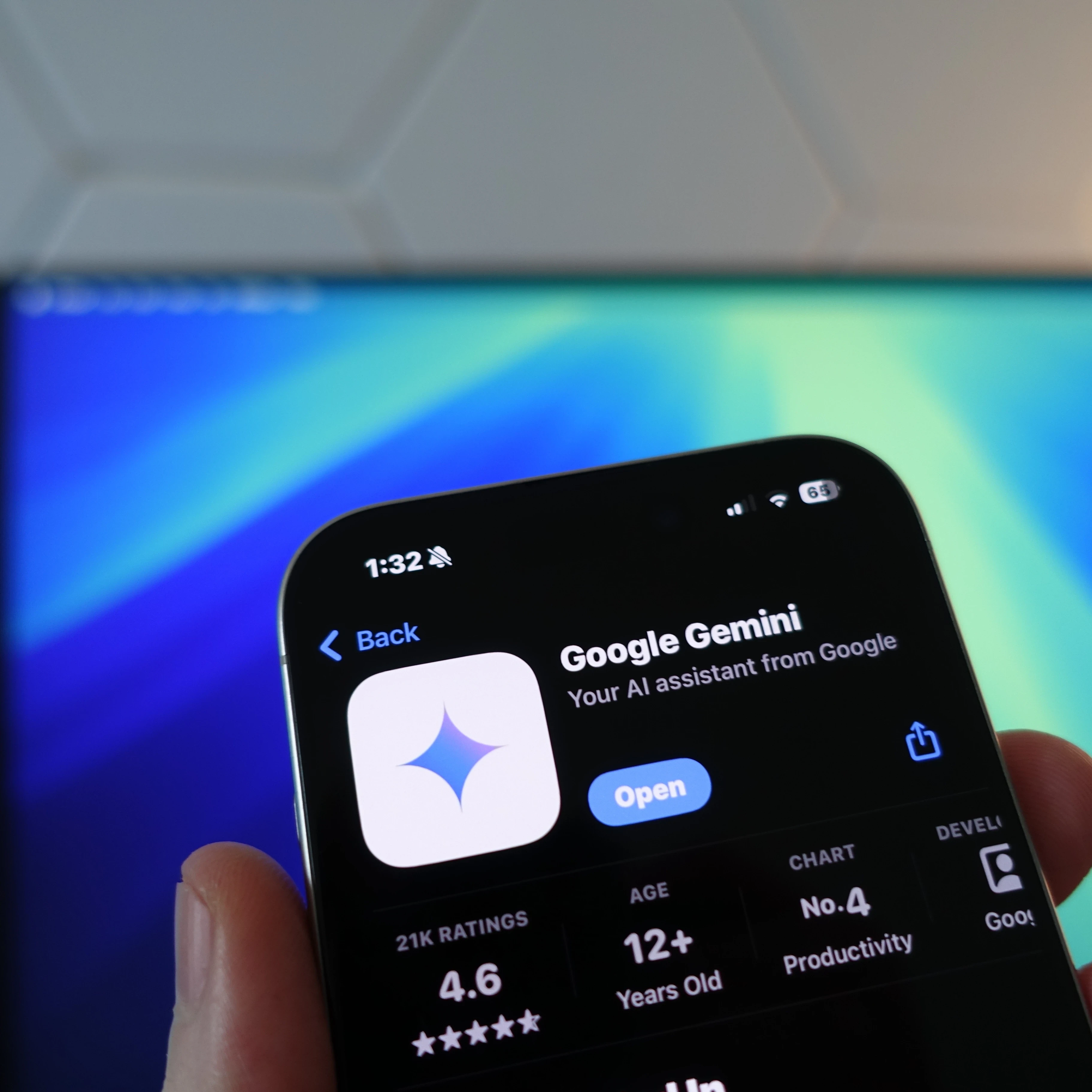 google gemini  app store screen on iphone in front of computer monitor with blue screensaver