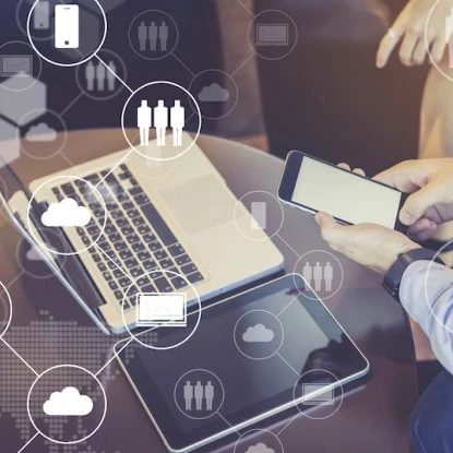 someone using a smartphone, with a macbook laptop and tablet next to them on a desk