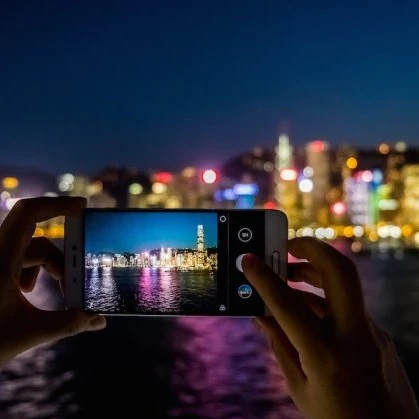 Person taking a photo using a smartphone of a China city skyline across the river at night