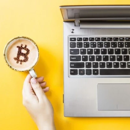 Coffee mug with Bitcoin latte art next to an Macbook laptop