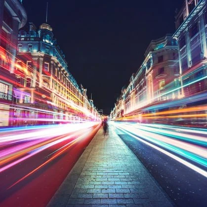 Person walking down Oxford Street with lights beaming past on either side