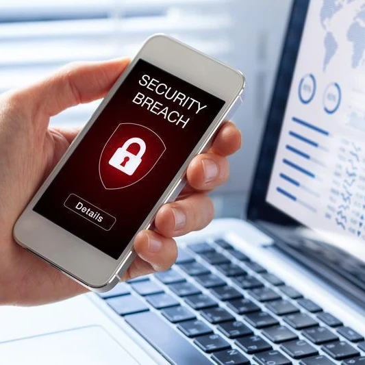 Person holding a smartphone with the words "Security Breach" and a lock in front of a laptop displaying graphs.