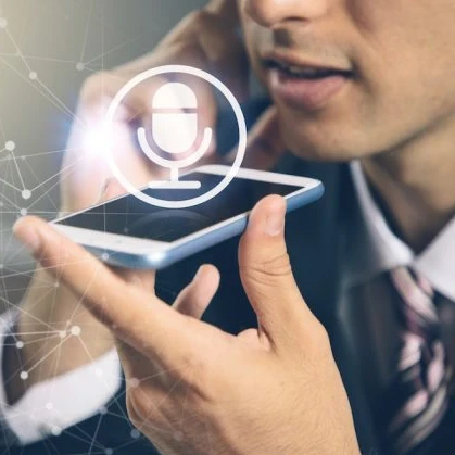 Image of someone speaking into a smartphone for voice to text with a microphone logo above the smartphone to highlight voice recognition