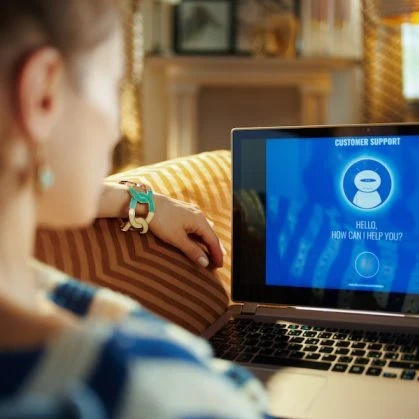 A woman sitting on a couch with a virtual customer support agent on a laptop.